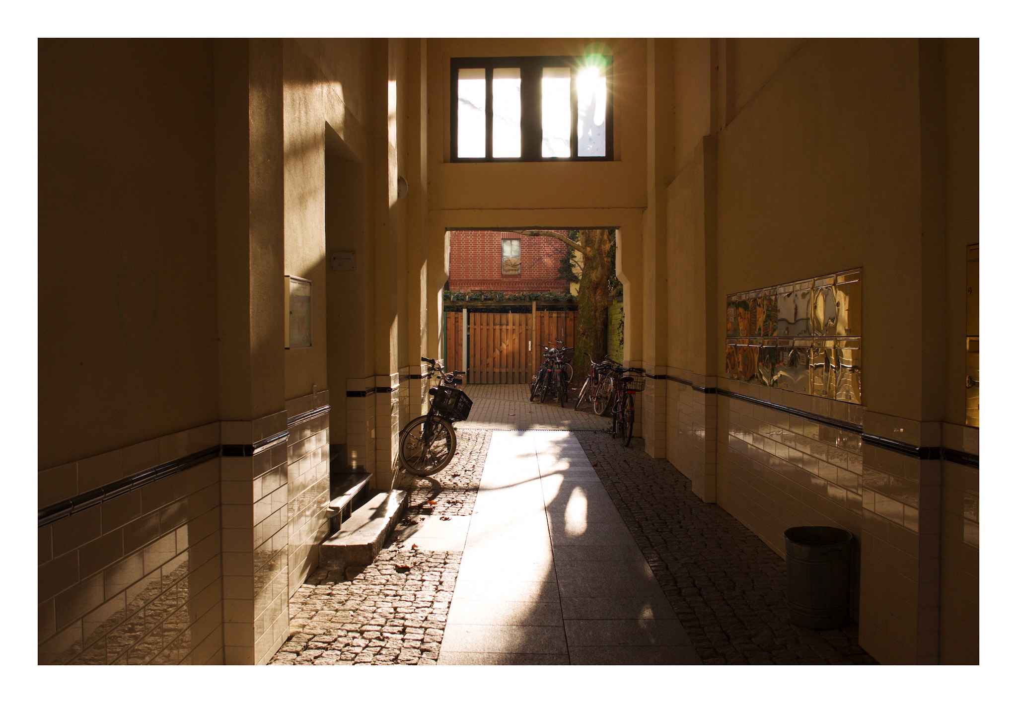 A photo of an entranceway, with mailboxes to the right, stairs to the left, and some bicycles leaning against the sides, with the sun beaming in with a little lens flare